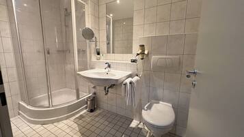 Un baño moderno con ducha de vidrio, lavamanos con espejo y retrete.