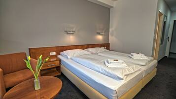 A hotel room with a bed, a wooden nightstand, a round table with a vase of flowers, and a brown sofa.