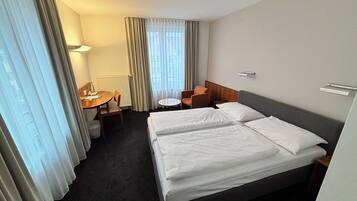A hotel room with two beds, a desk, a chair, a small table, and a window with curtains.