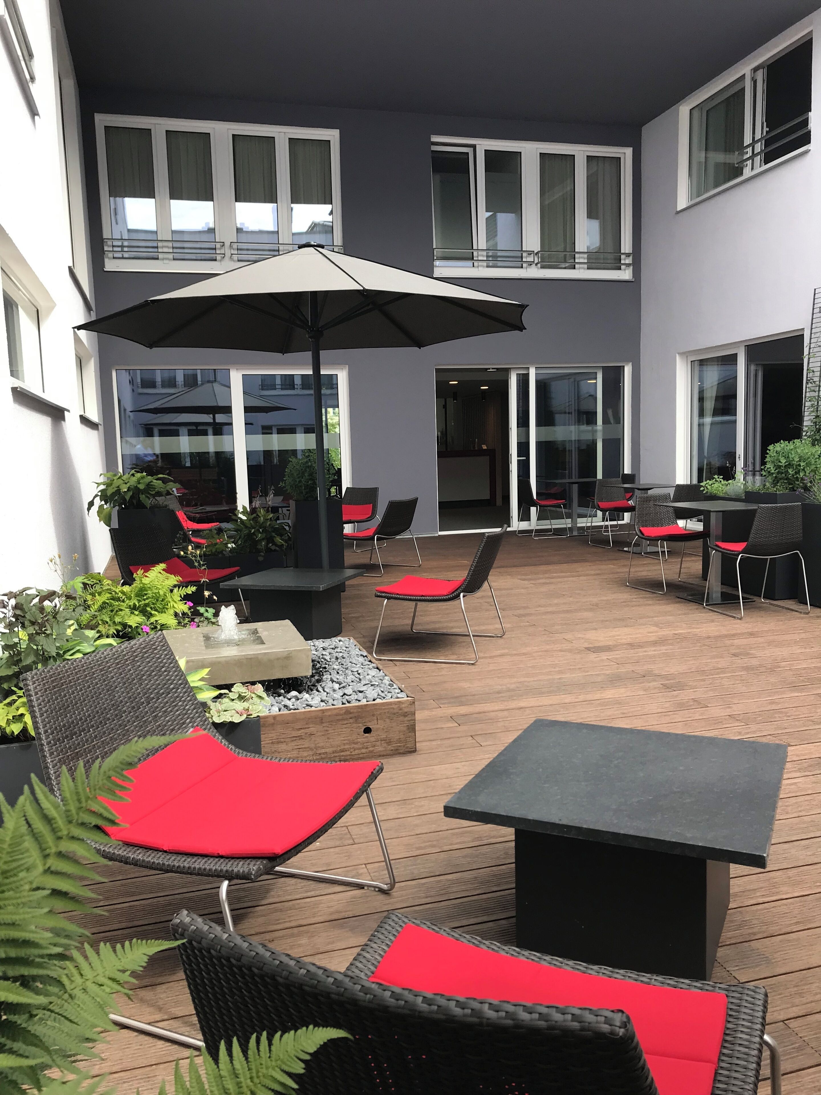 Eine Terrasse im Freien mit Korbmöbeln, roten Kissen und einem schwarzen Sonnenschirm.