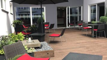 Eine Terrasse im Freien mit Korbmöbeln, roten Kissen und einem schwarzen Sonnenschirm.