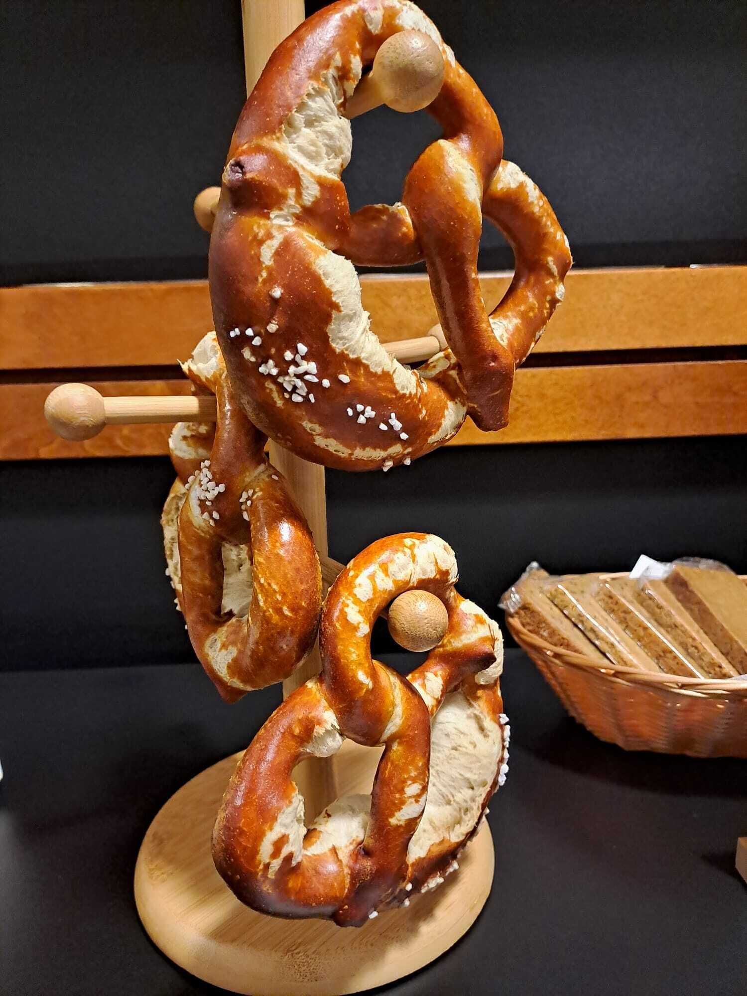 Un pretzel sobre un soporte de madera, con una cesta de pretzels en rodajas al fondo.