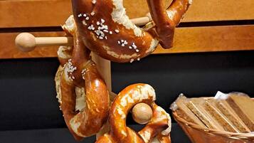 Un pretzel sobre un soporte de madera, con una cesta de pretzels en rodajas al fondo.