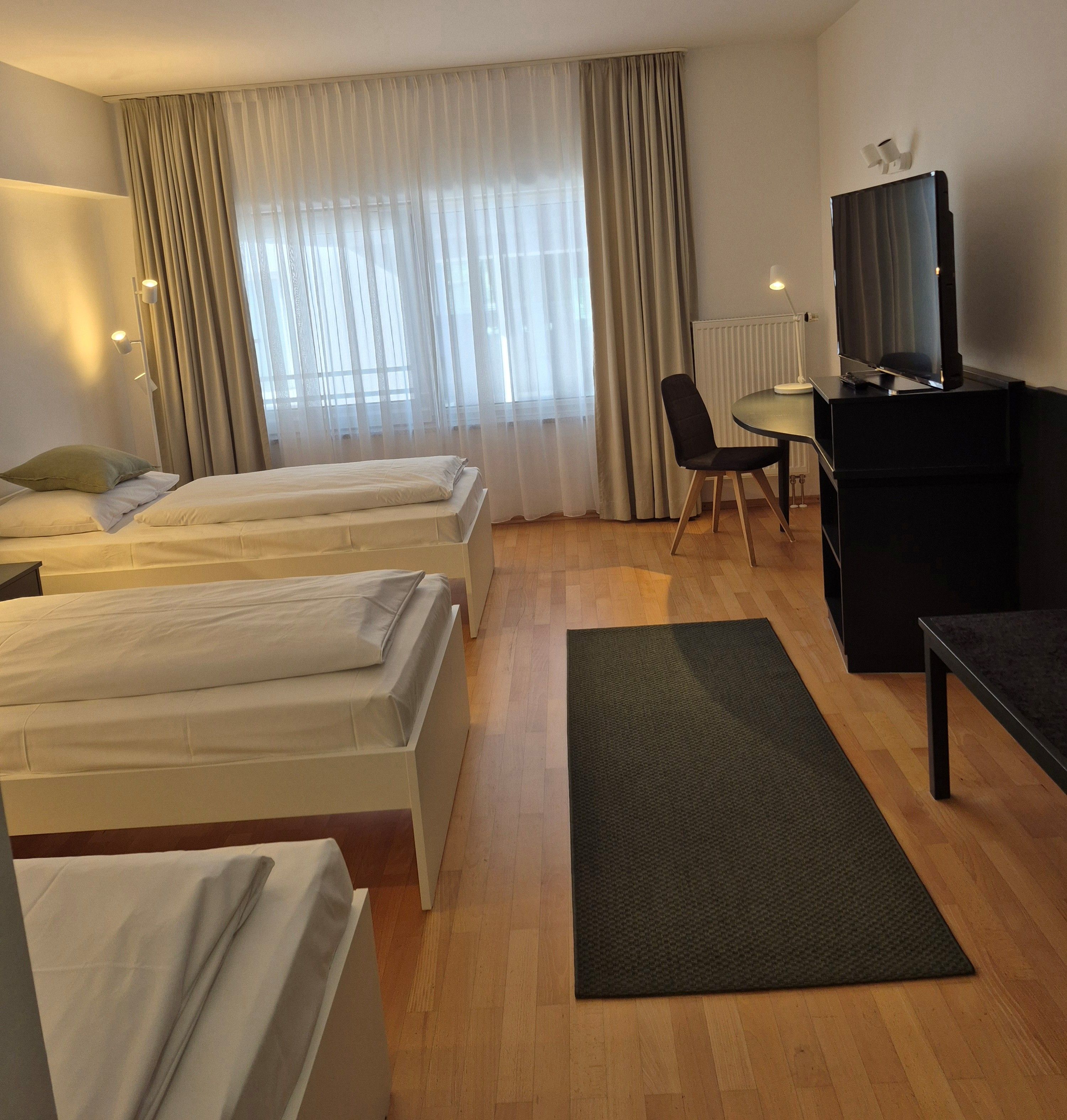 Habitación de hotel con dos camas, un escritorio, una silla, un televisor y una ventana con cortinas.