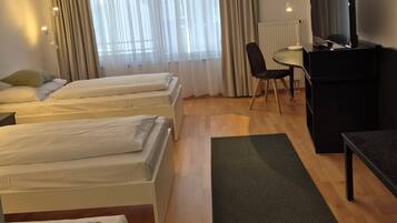 Habitación de hotel con dos camas, un escritorio, una silla, un televisor y una ventana con cortinas.