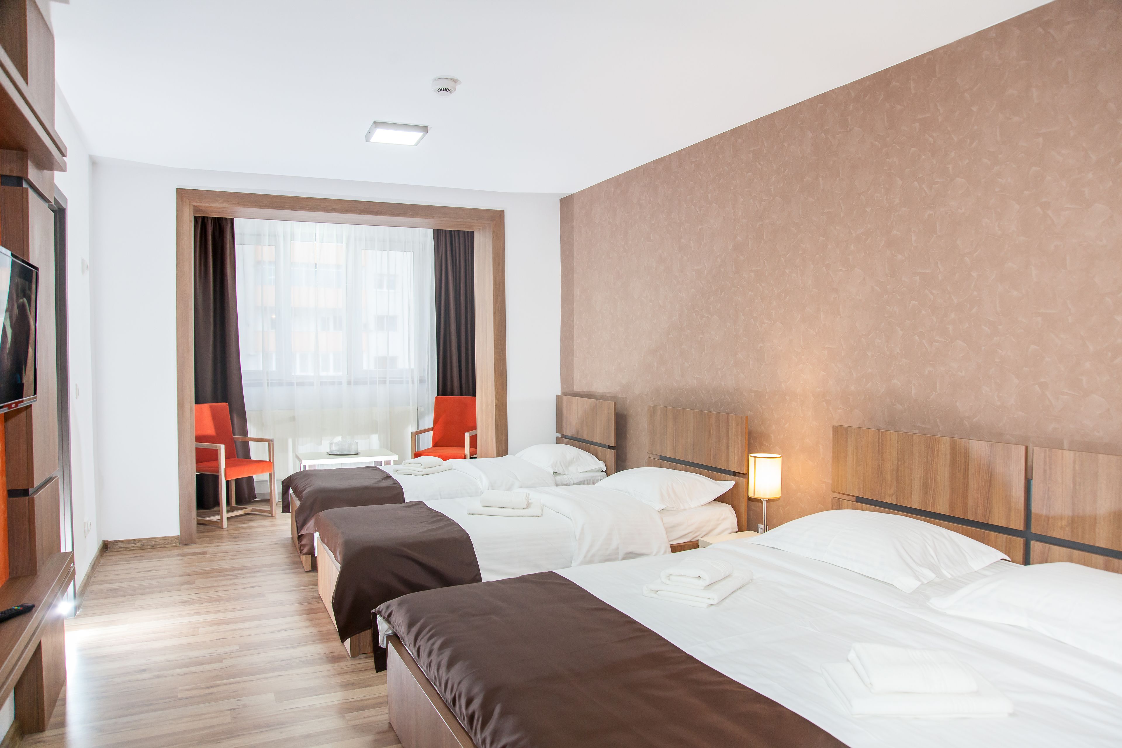 Ein Hotelzimmer mit zwei Betten, einem Fernseher, einem Schreibtisch und einem Fenster mit Vorhängen.