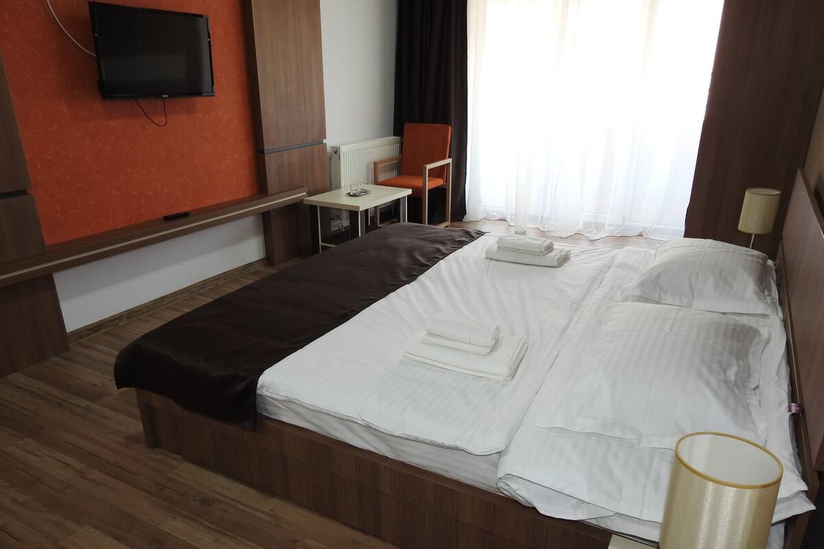 Una habitación de hotel con cama, mesita de noche, lámpara y televisor montado en la pared.