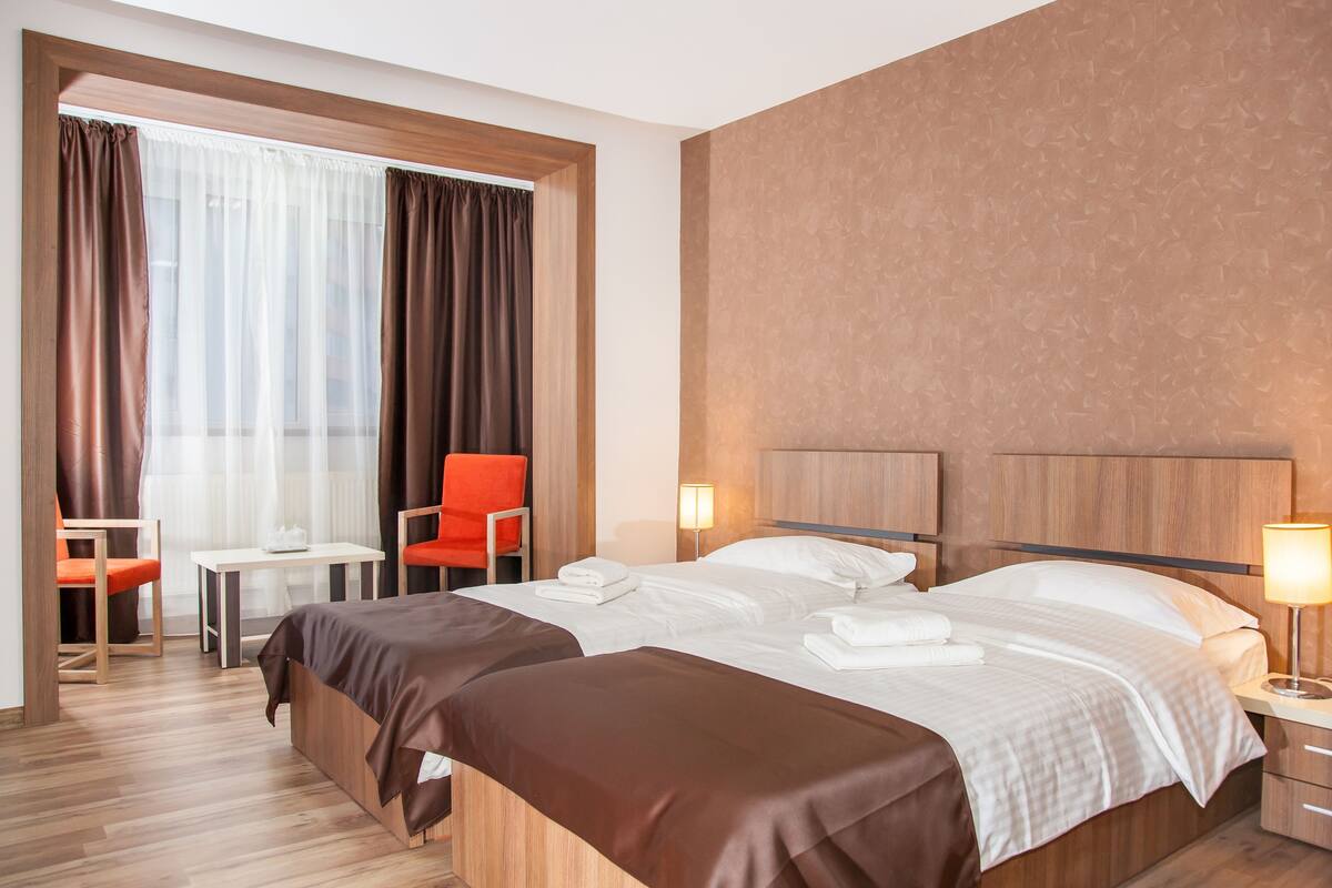 Habitación de hotel con dos camas, un escritorio, sillas y una ventana con cortinas.