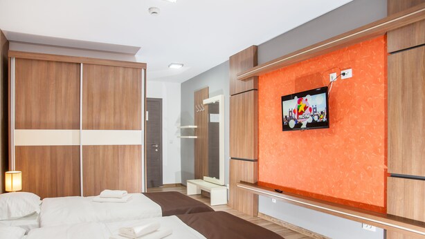 Habitación de hotel con dos camas, un televisor instalado en una pared naranja y armarios de madera.