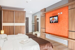 A hotel room with two beds, a TV mounted on an orange wall, and wooden wardrobes. - HB Brilliant (Brasov)