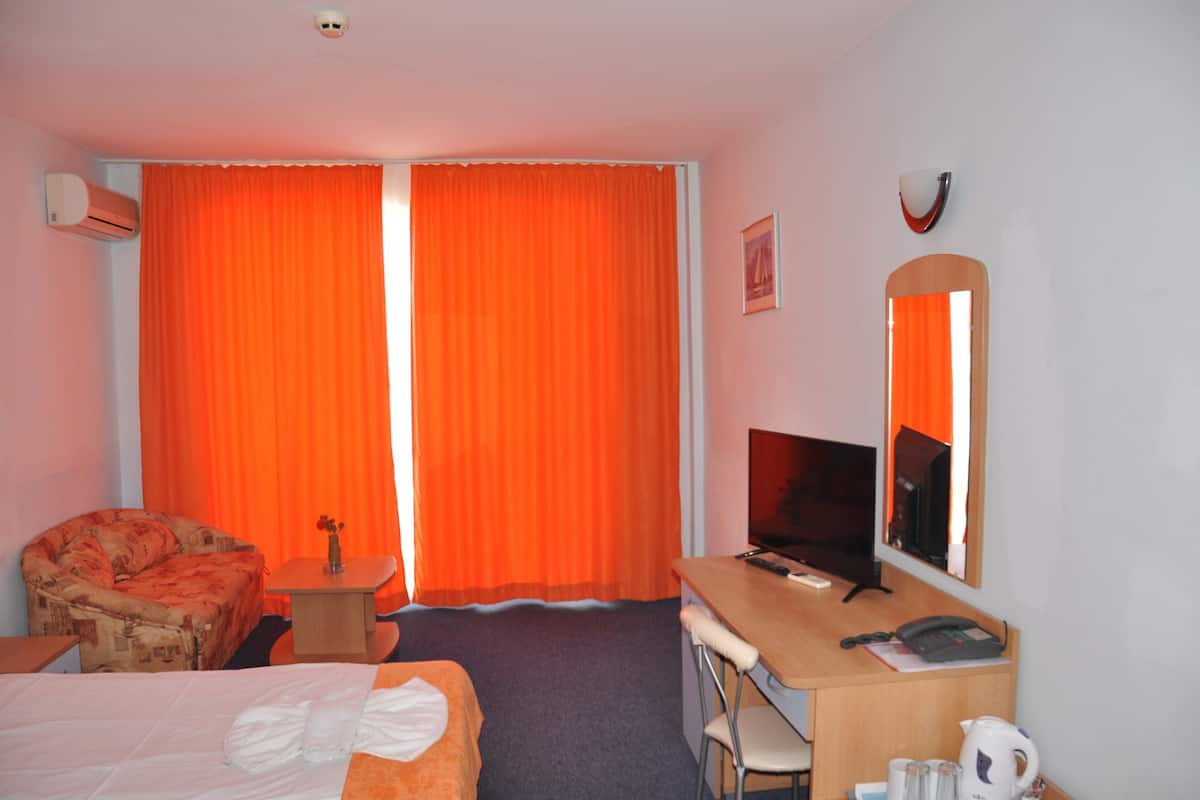 A hotel room with a bed, a desk, a chair, a television, and an air conditioning unit.