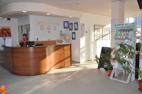 A reception area with a wooden desk, a clock, and framed pictures on the wall. - Hotel BelleVille (Sunny Beach)