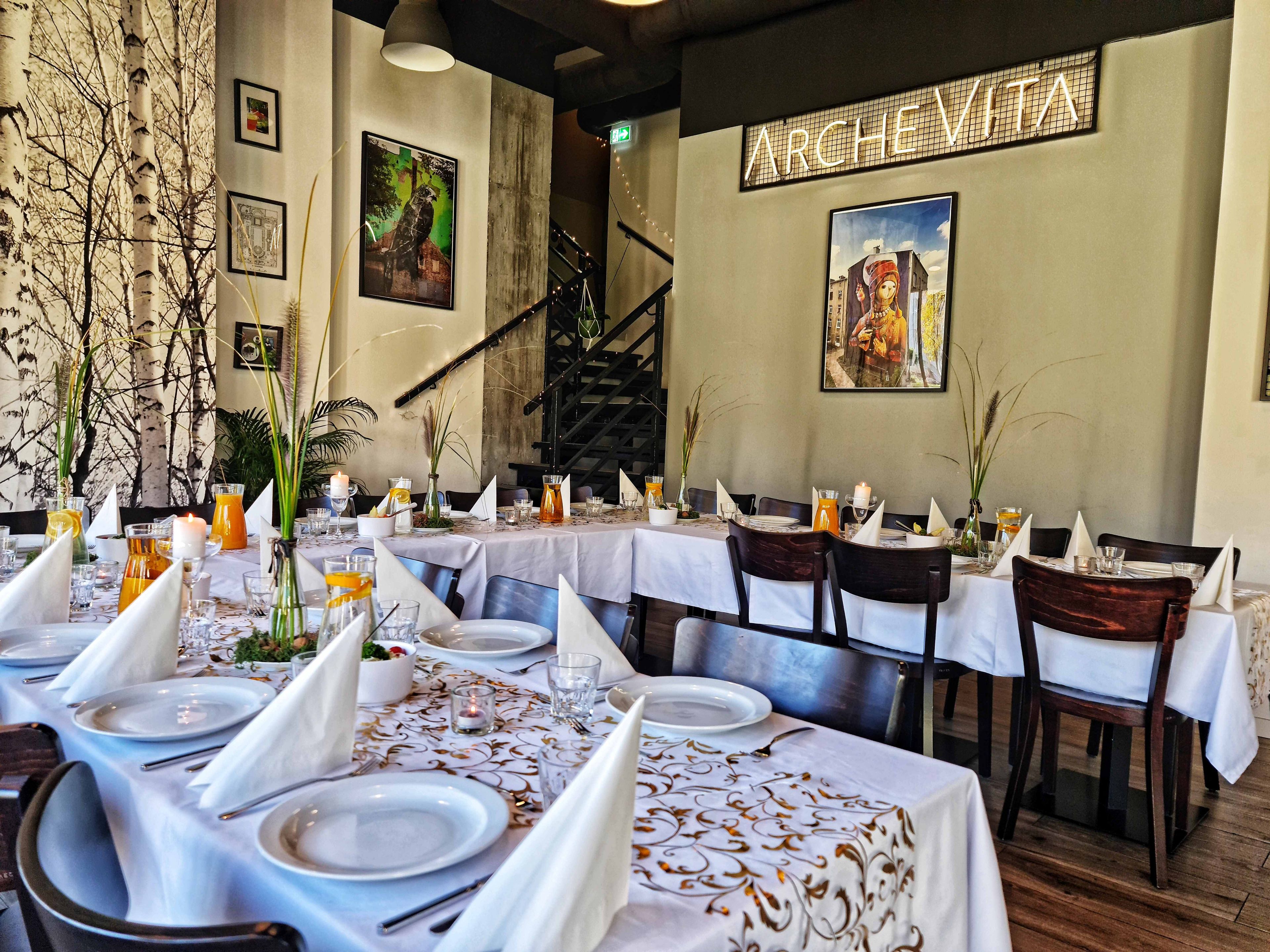 A restaurant with tables set for dining, framed artwork on the walls, and a staircase in the background.