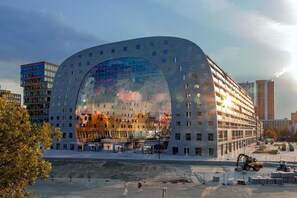 A modern building with a large glass facade and a curved roof, surrounded by construction equipment and other buildings.