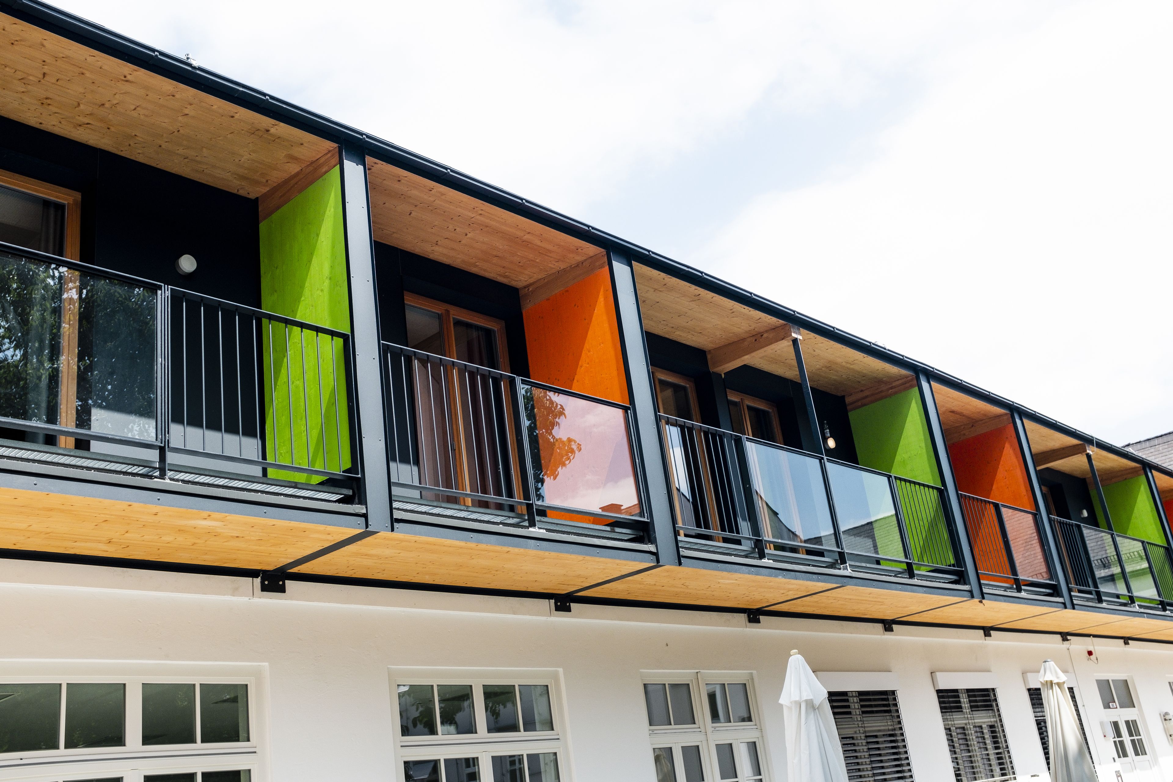 Un edificio de varios pisos con balcones, ventanas grandes y una terraza de madera.