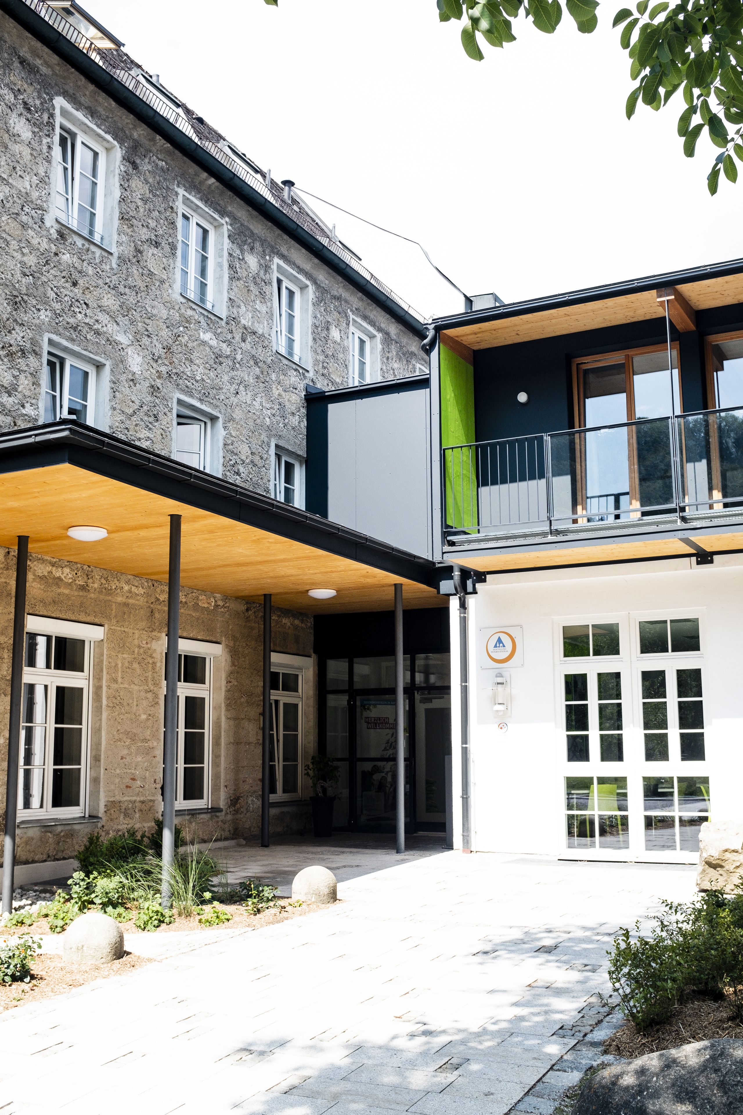 A building with a stone facade, a covered entrance, and a balcony with a railing.