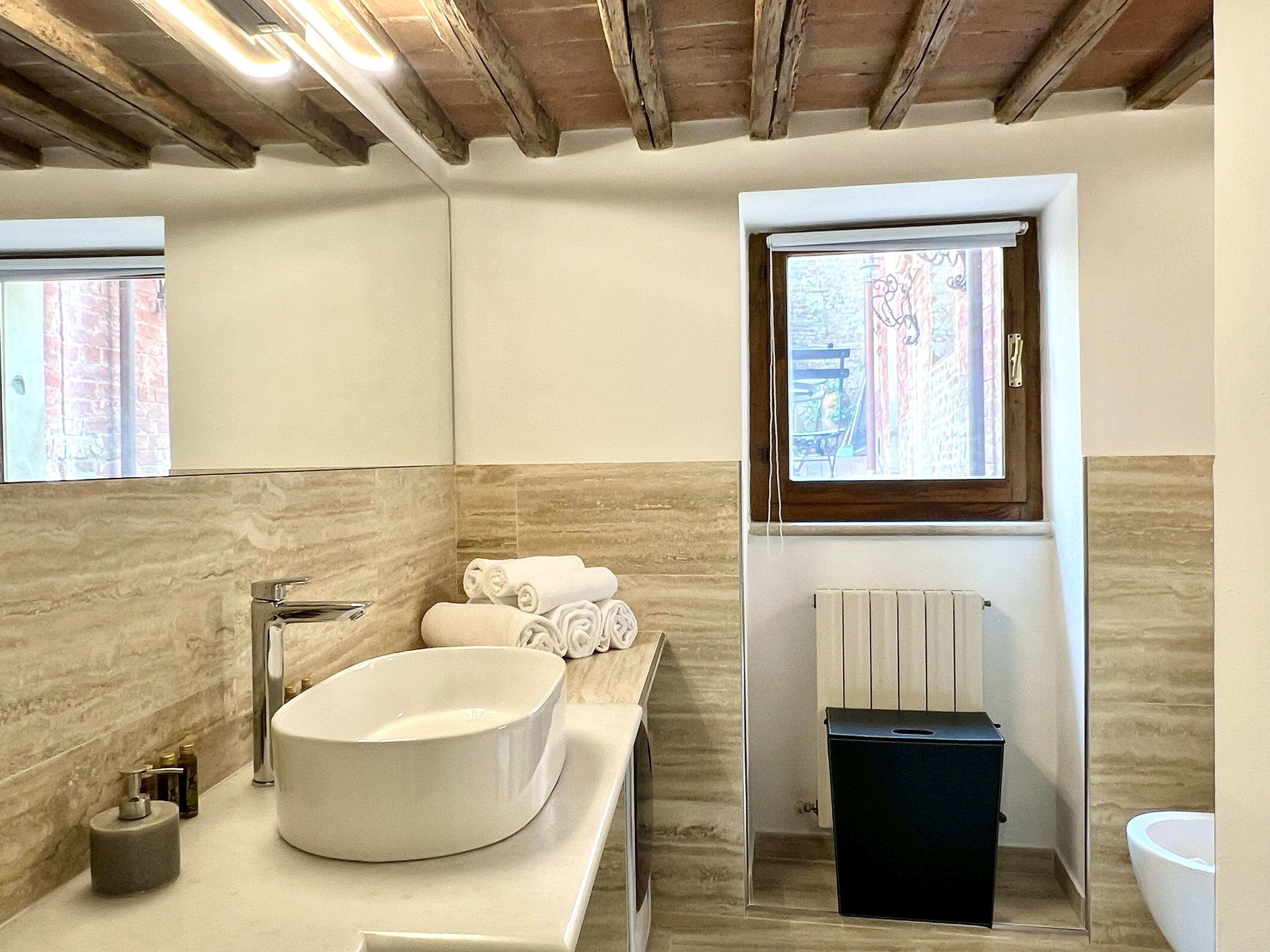 A modern bathroom with a large oval sink, a mirror, a window, and a radiator.
