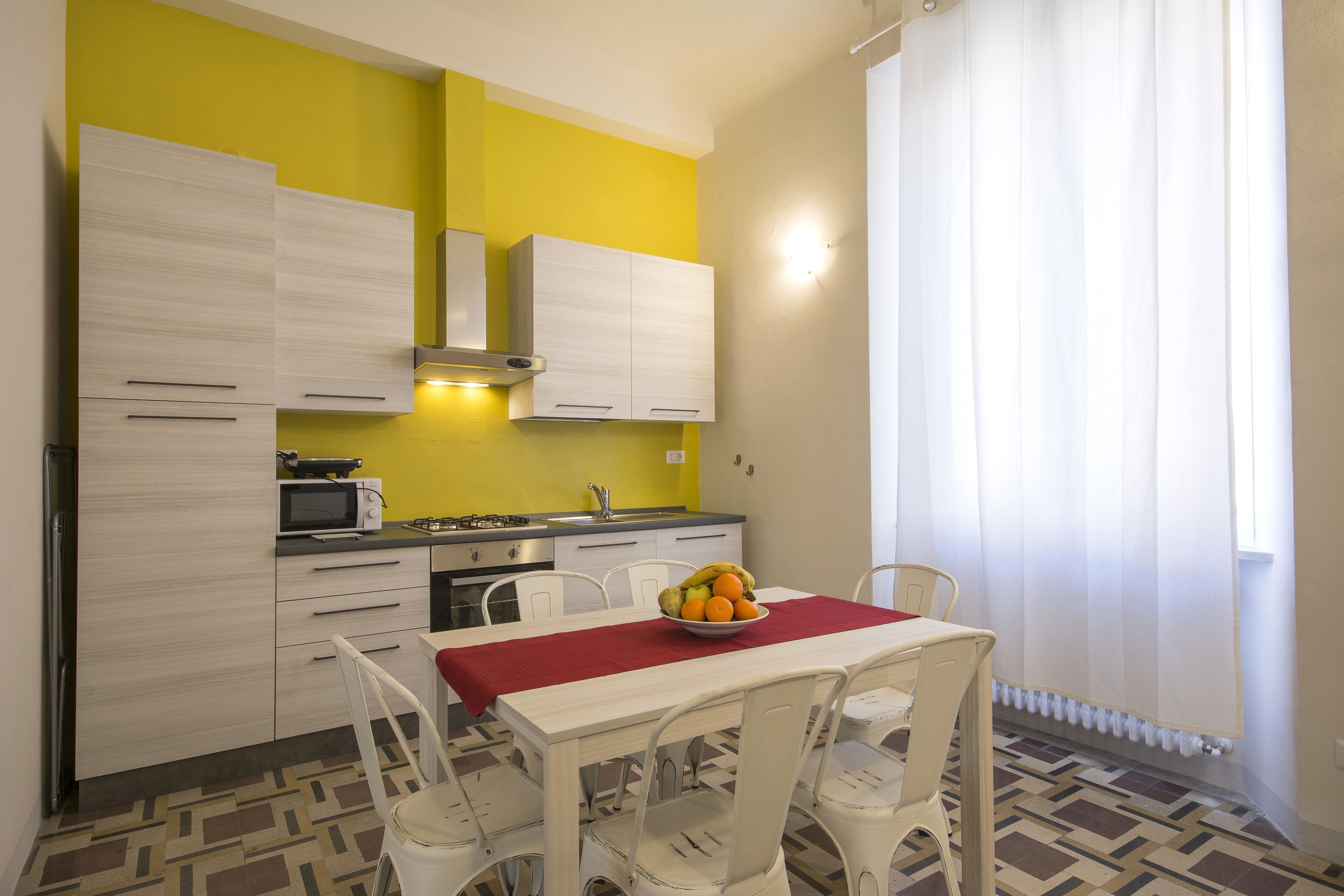 A kitchen with white cabinets, a microwave, and a fruit bowl on the table.