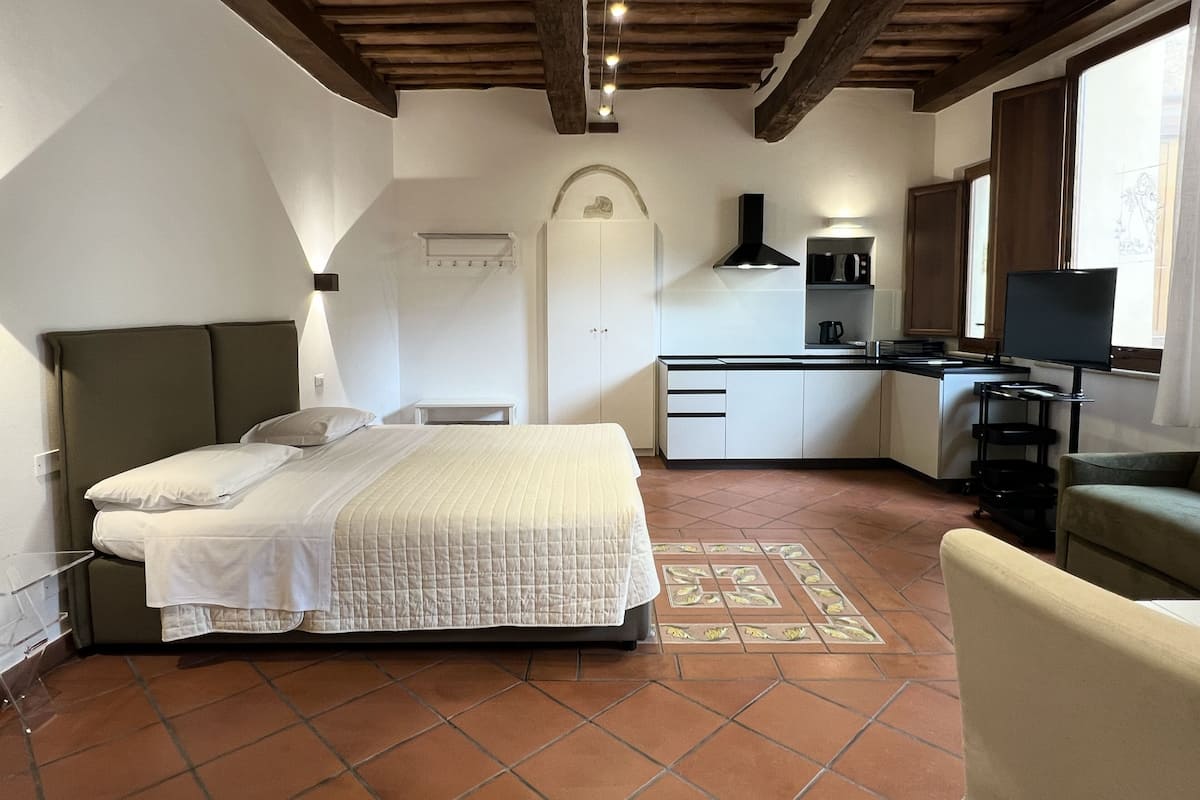 A bedroom with a bed, a desk, a chair, and a kitchenette.