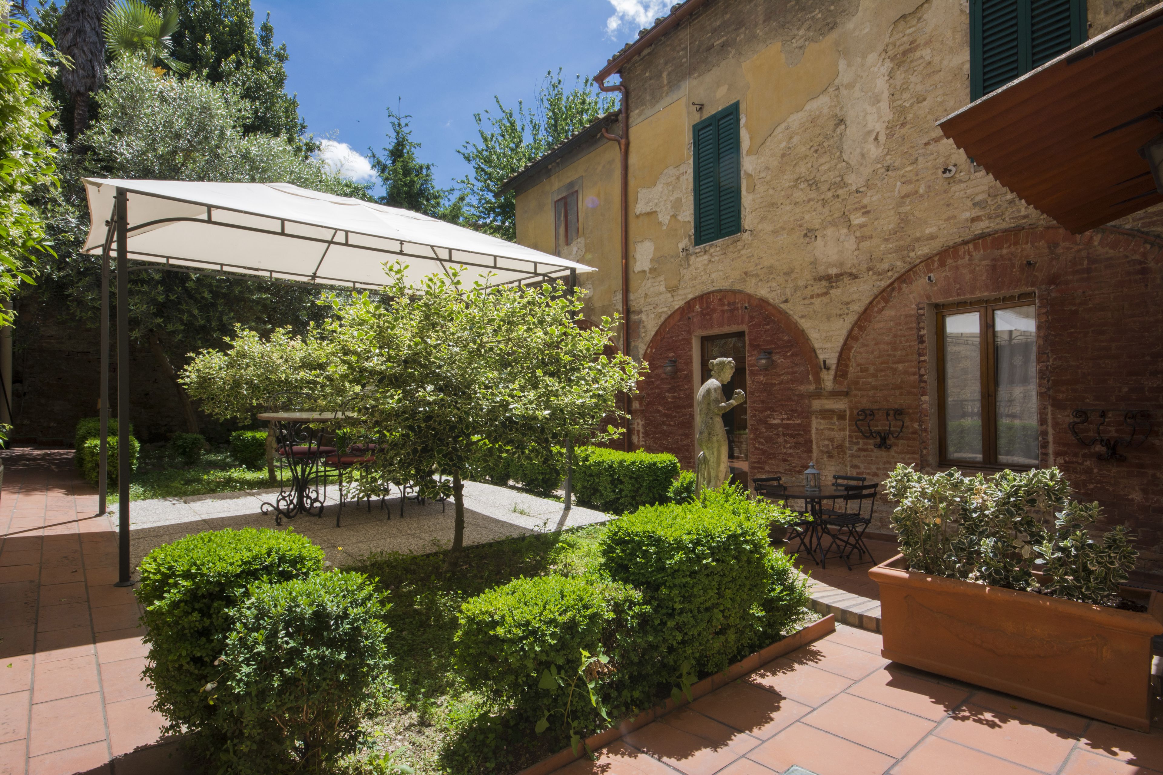 Un cortile con un'area salotto coperta, una statua e un edificio con finestre ad arco.