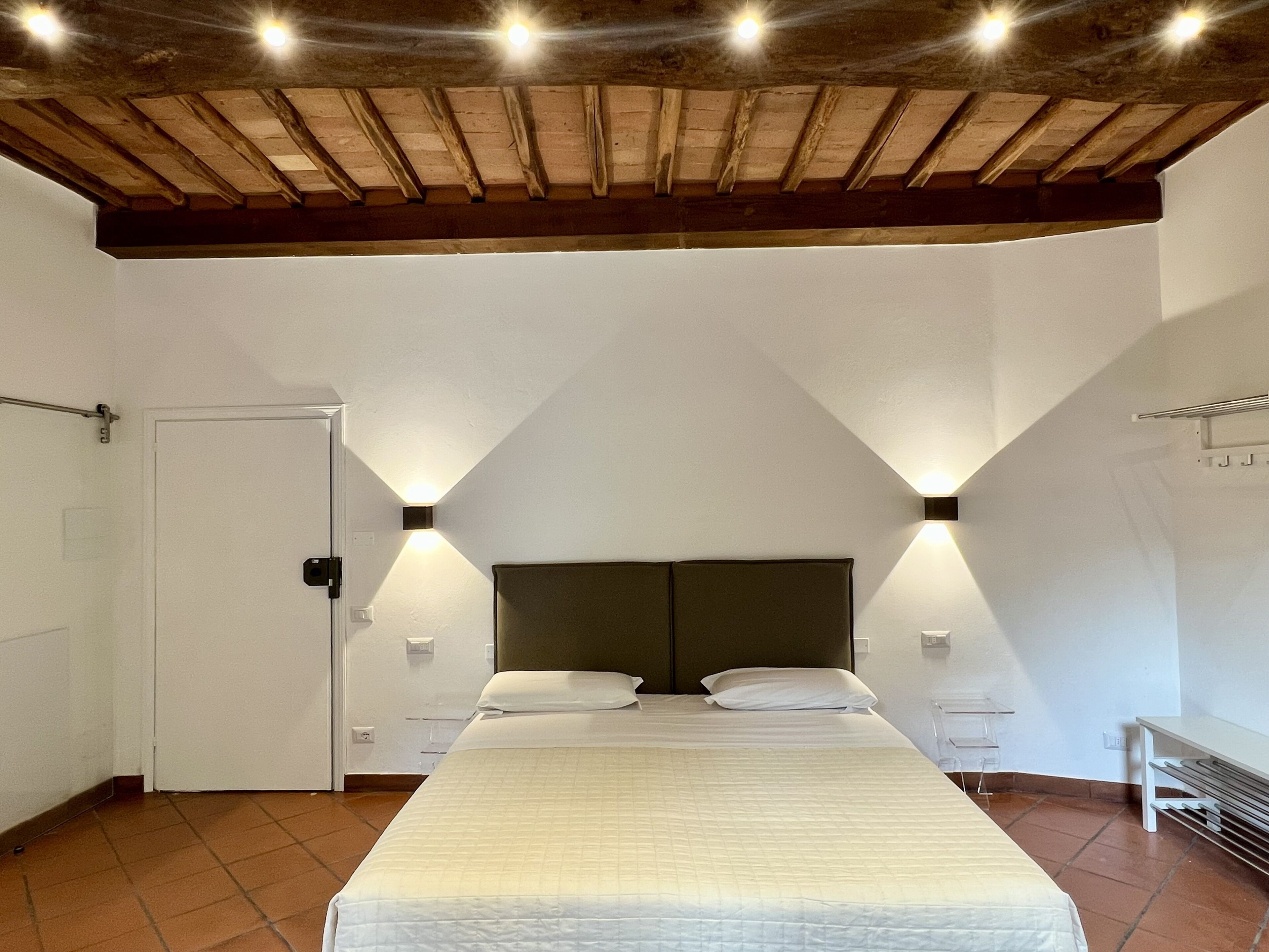 A bedroom with a large bed, two bedside tables, a wooden ceiling, and a door.