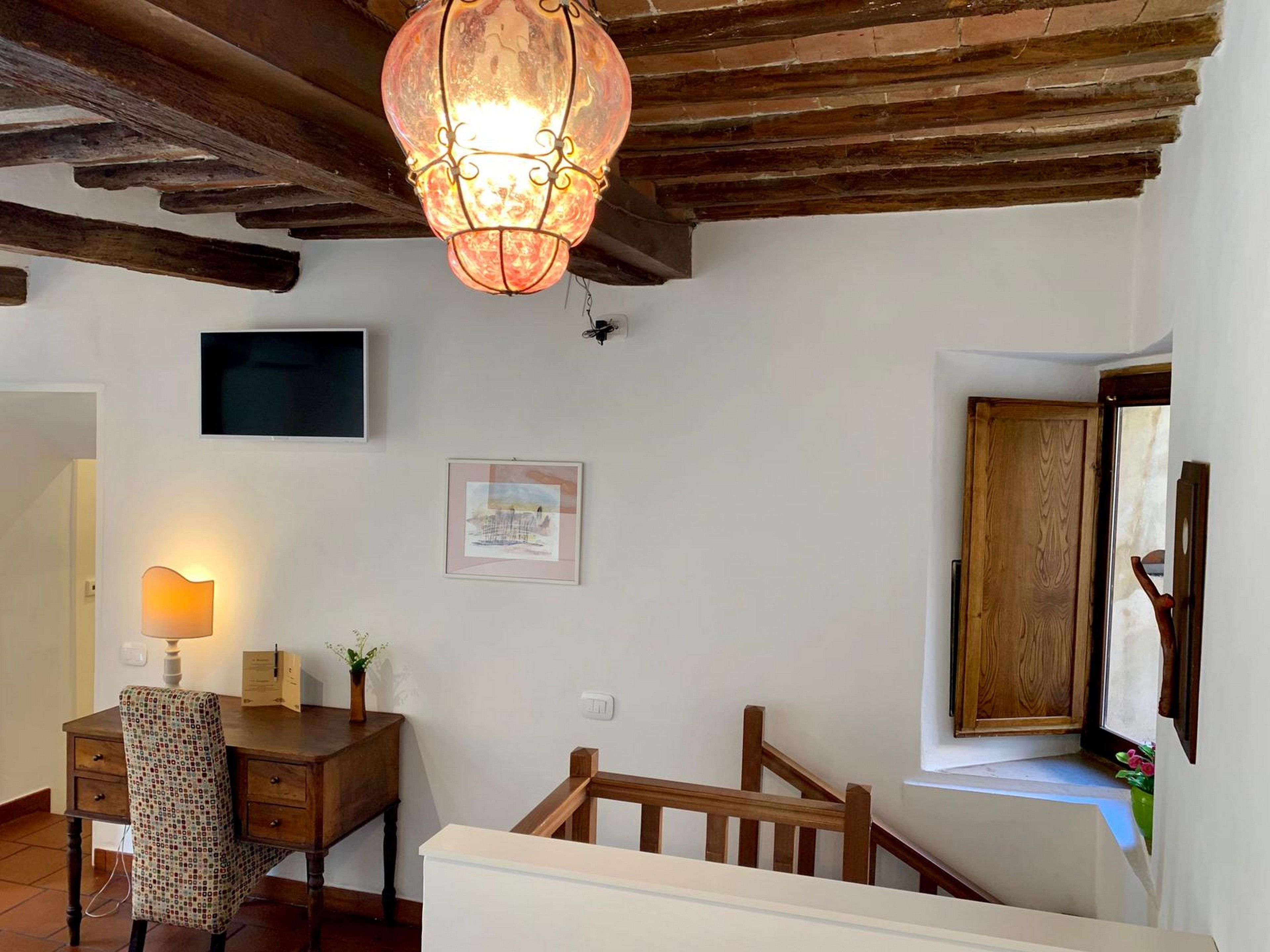 Ein Zimmer mit Holzboden, einem Schreibtisch mit Stuhl, einem Wand-Fernseher, einem gerahmten Bild und einem Fenster mit Holztür.