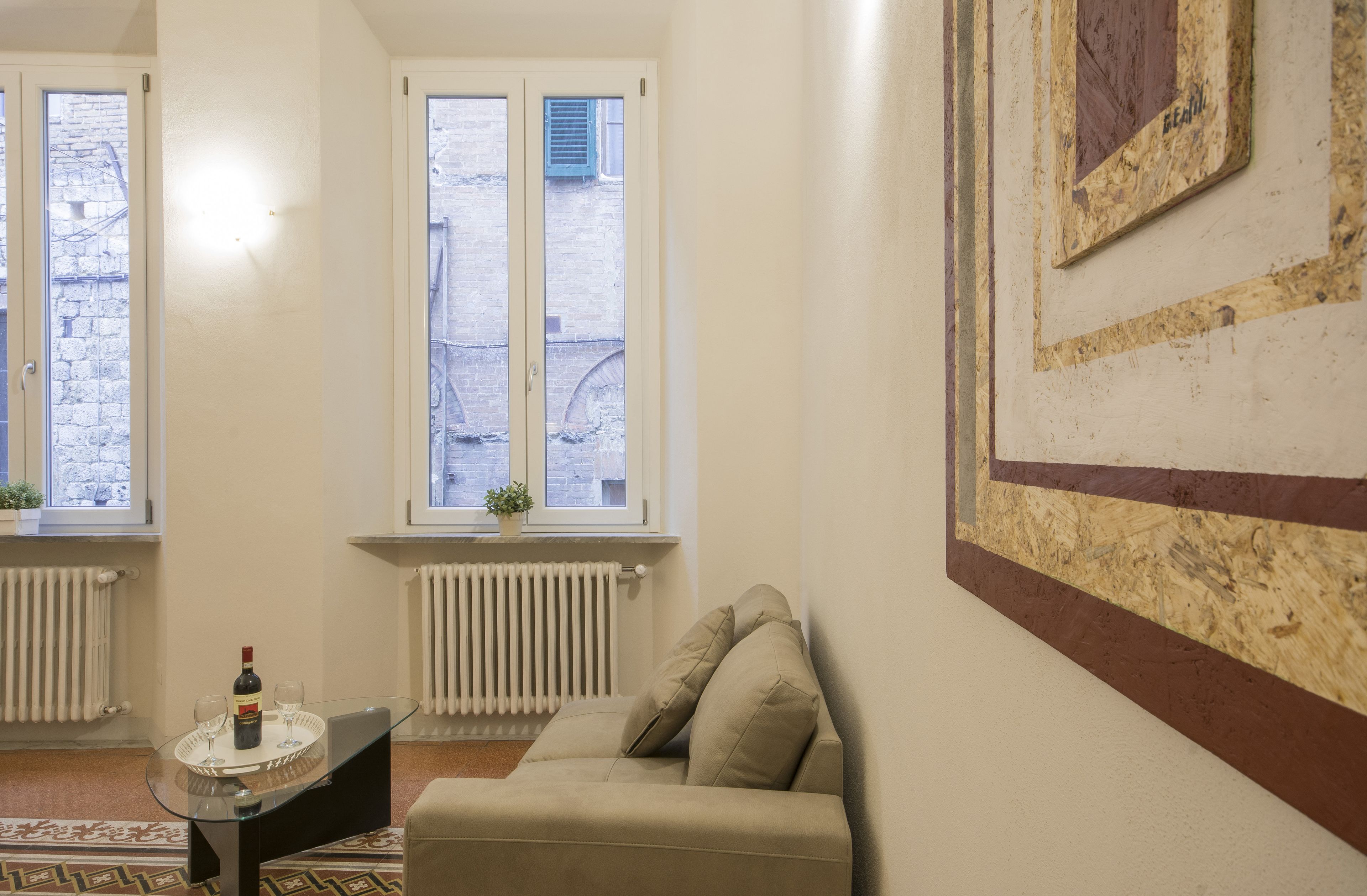 A room with a sofa, a small table with a bottle and glass, and two windows with shutters.