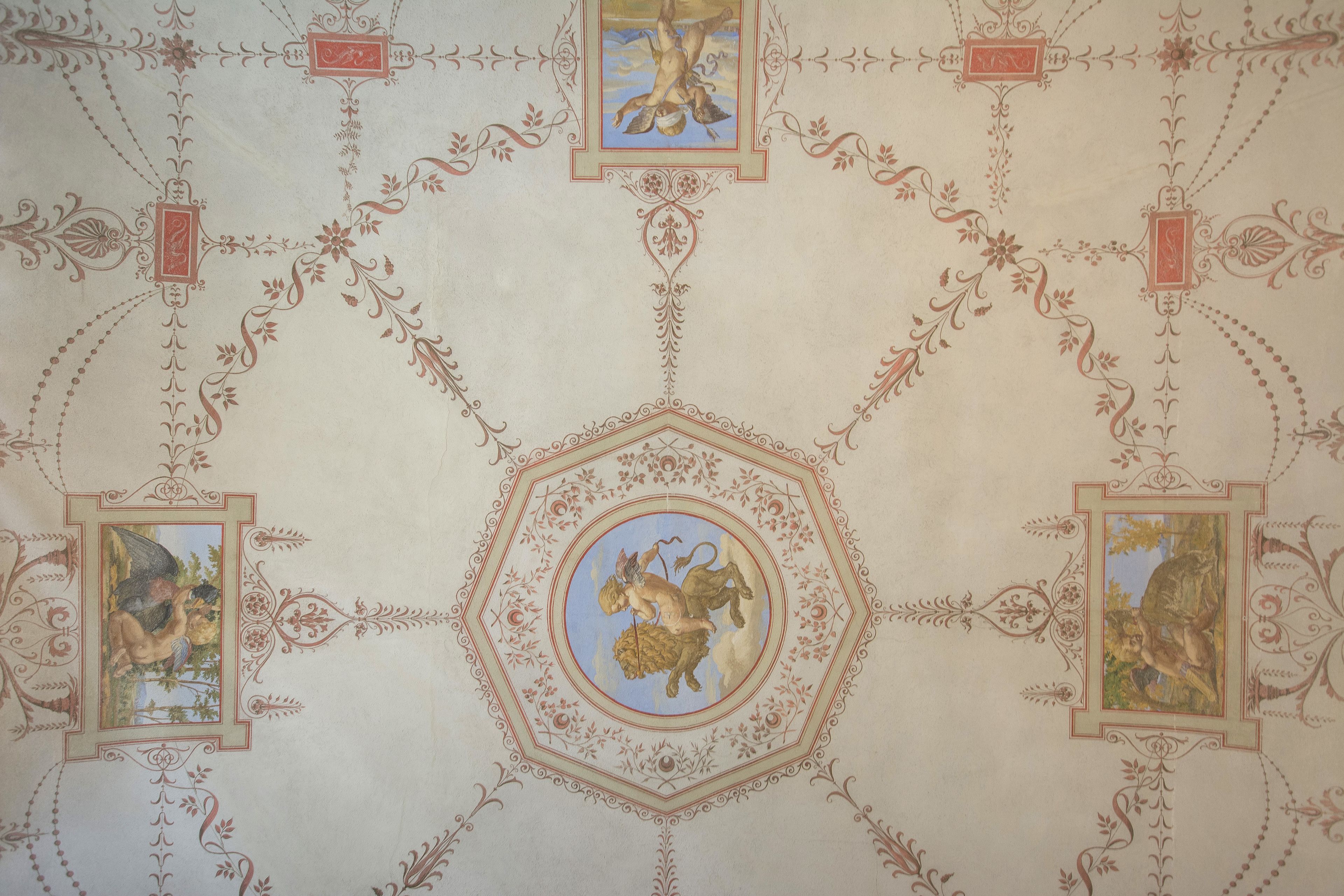 A ceiling with intricate floral and geometric patterns, including central medallions and framed images.