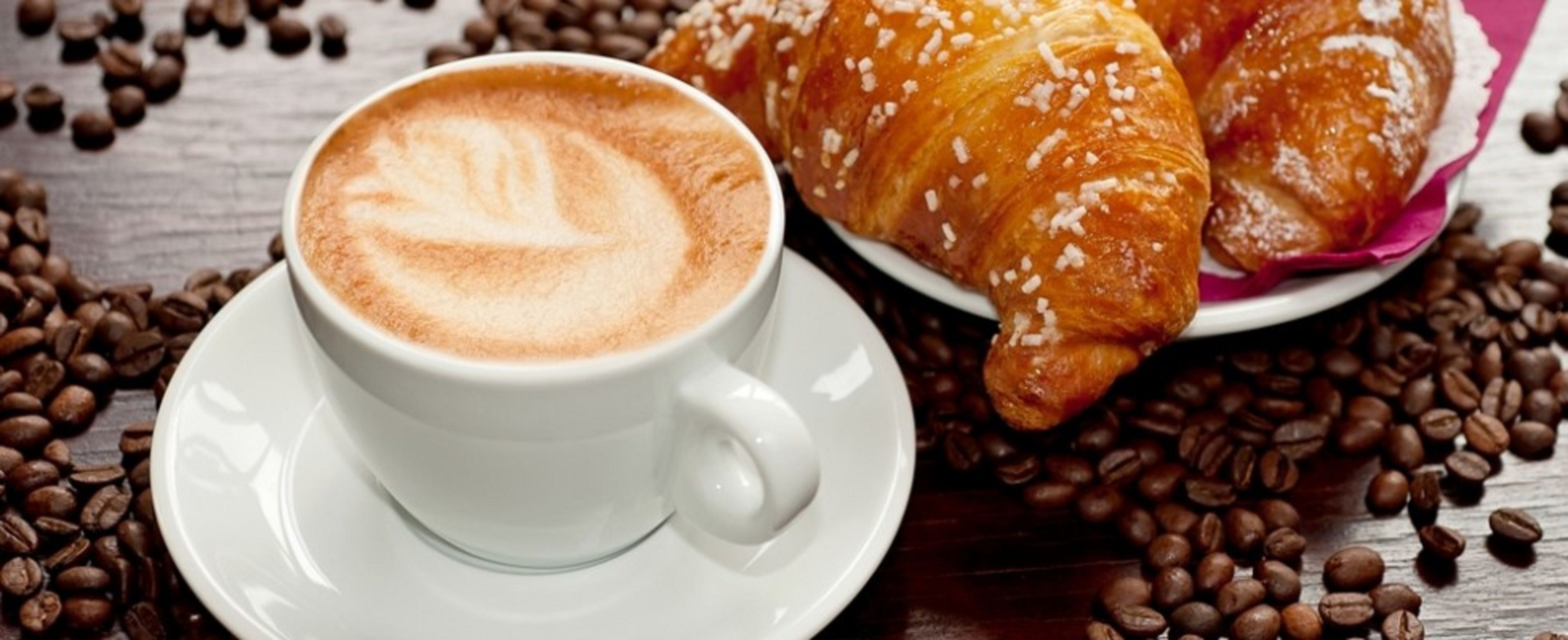 Una taza de café con arte de latte sobre un platillo rodeado de granos de café.