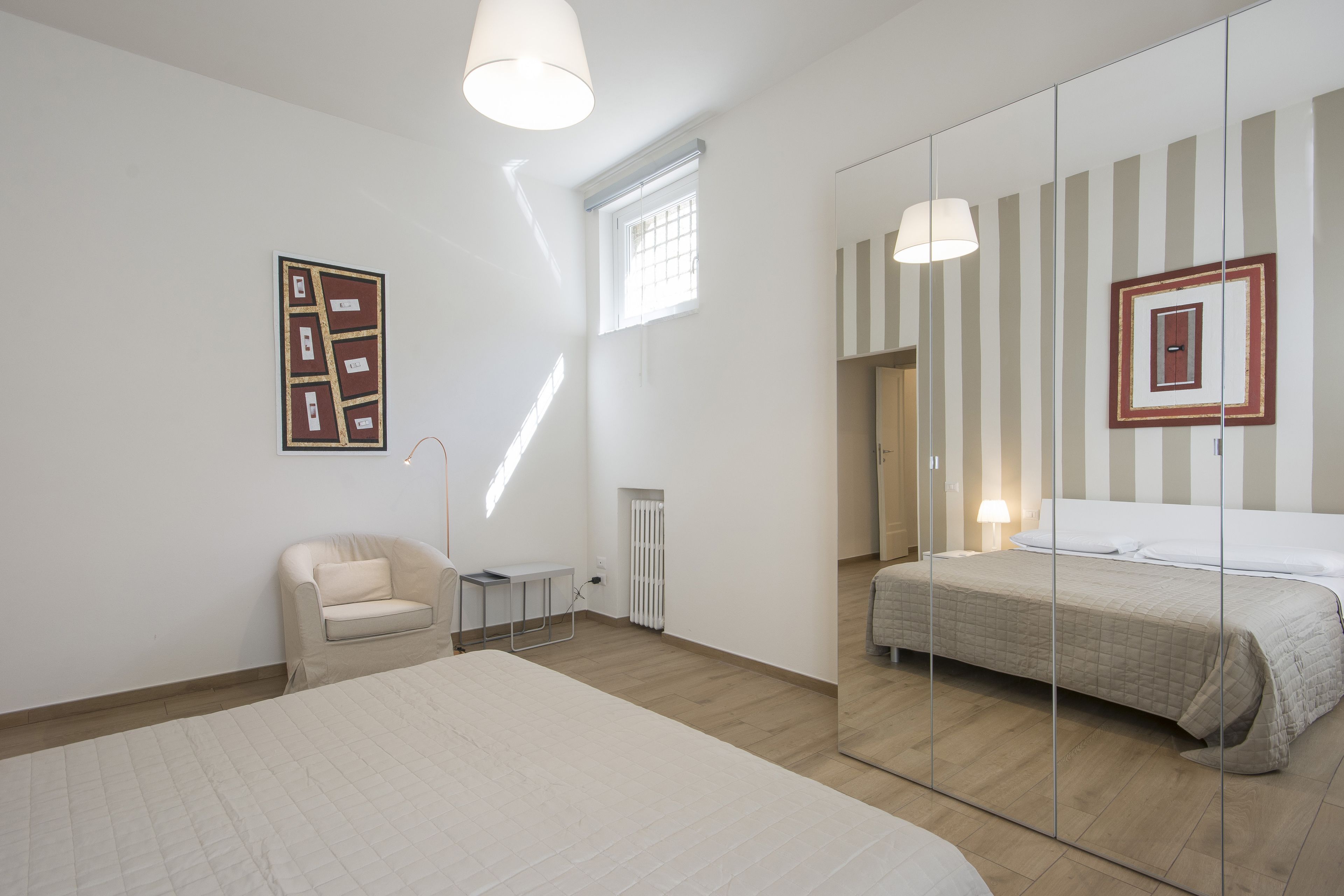A bedroom with a large bed, a small chair, a bedside table, a radiator, and a window.