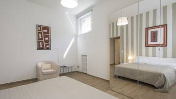 A bedroom with a large bed, a small chair, a bedside table, a radiator, and a window.