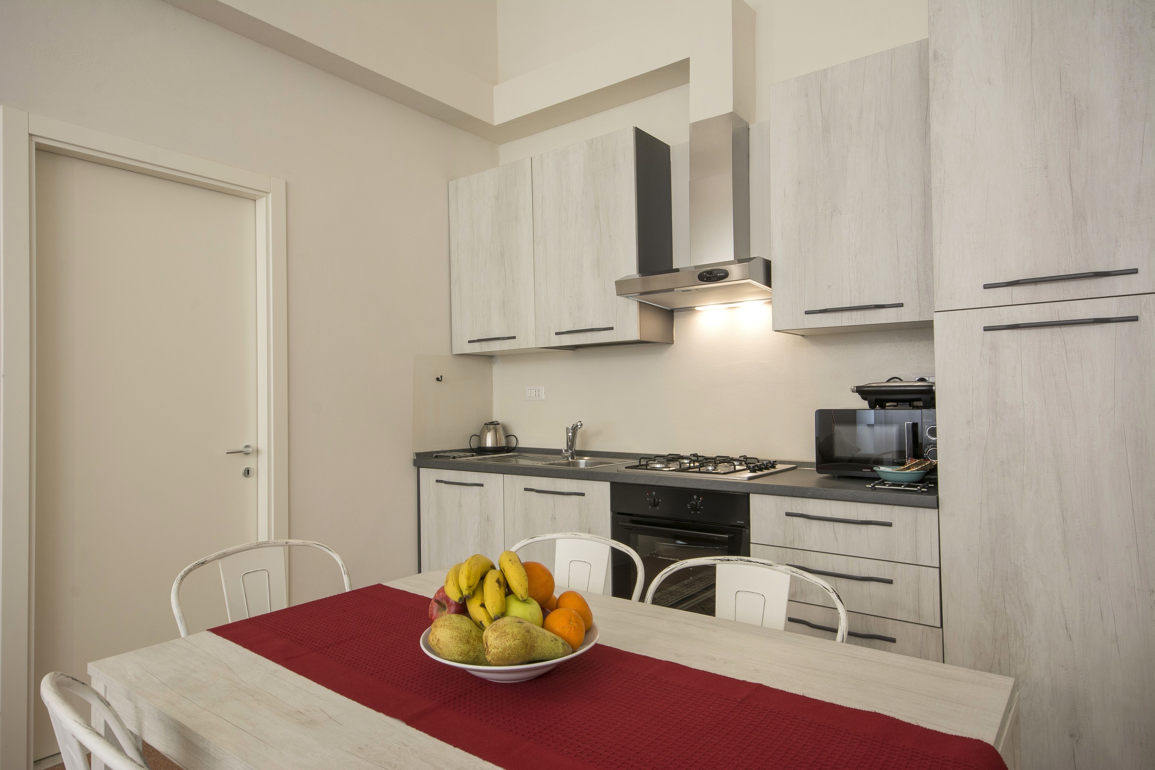 Een moderne keuken met witte kastjes, een gasfornuis, een magnetron, en een fruitschaal op de eettafel.