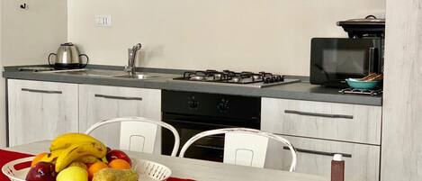 A compact kitchen with white cabinets, a gas stove, a sink, and a dining table with a red tablecloth.