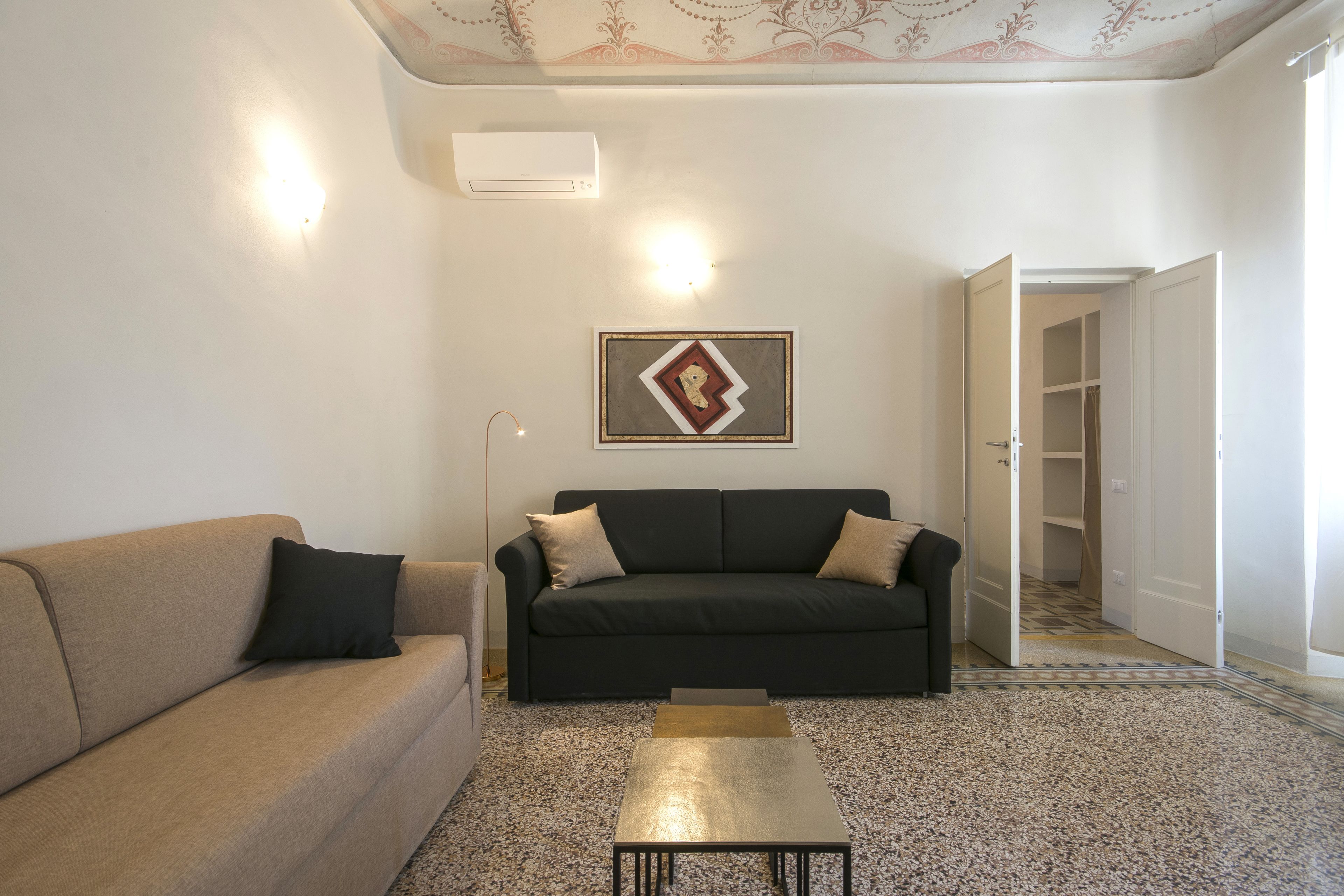 Un salon avec un canapé beige, un canapé foncé et une table basse. Un tableau encadré est accroché au mur, et une porte donne accès à un placard.