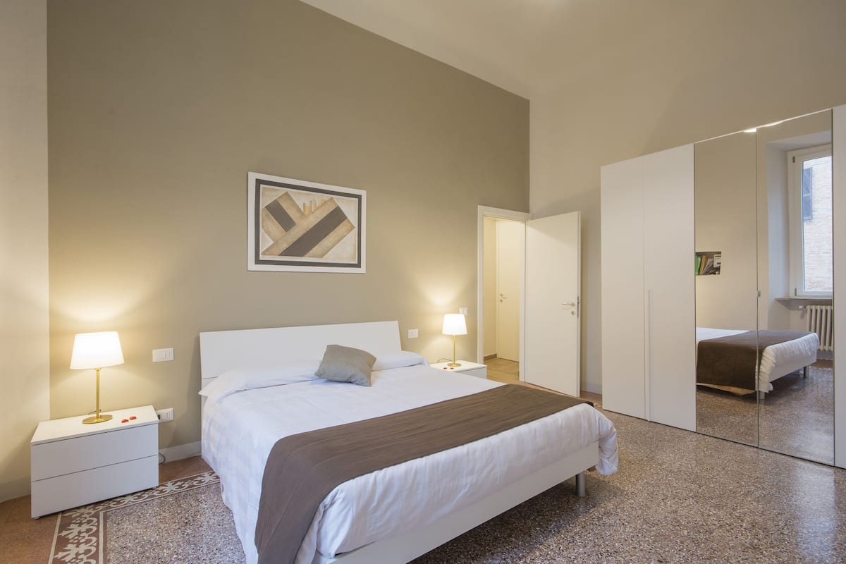 A hotel room with a bed, bedside tables, a mirror, and a wall-mounted artwork.