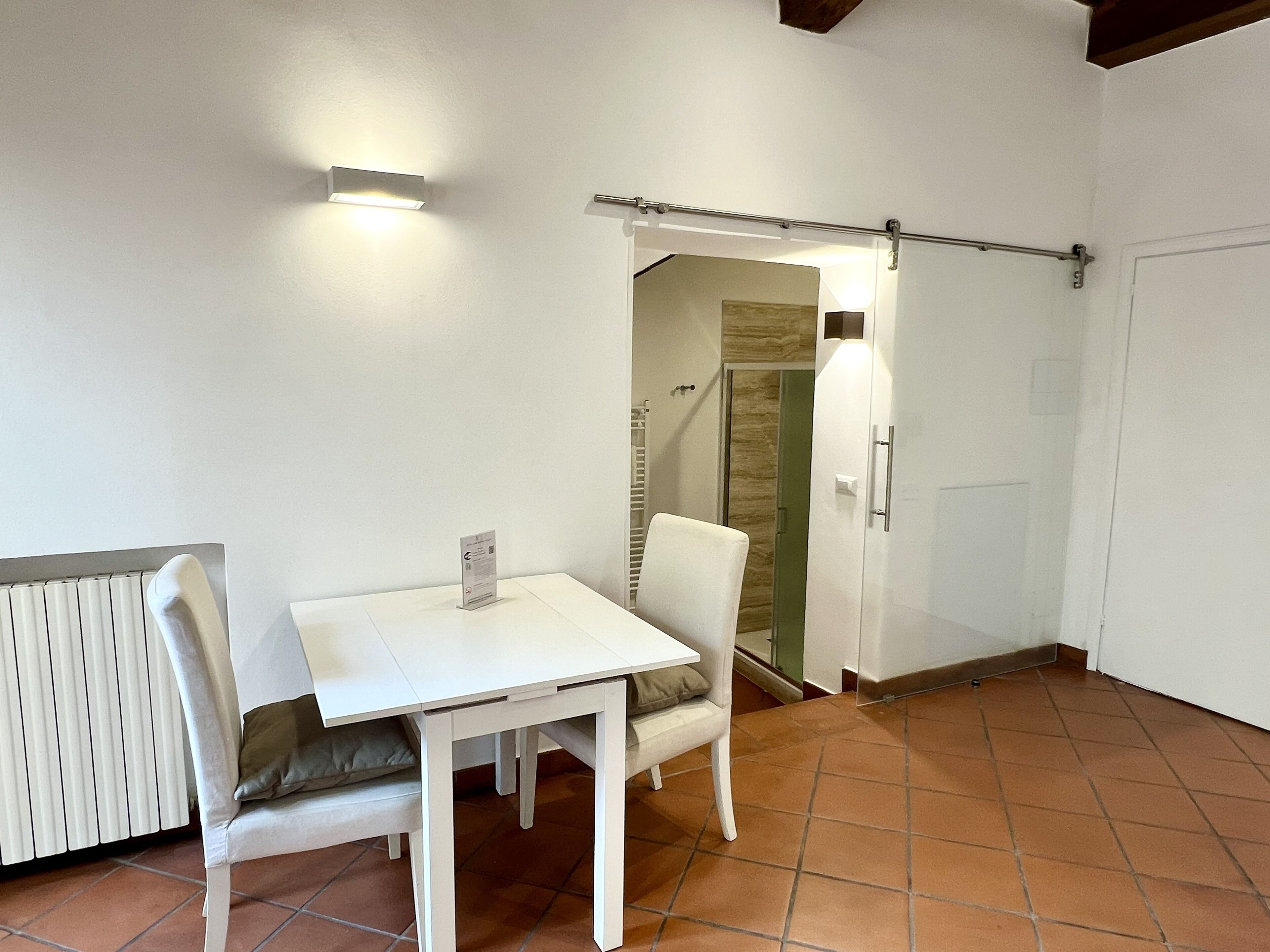 A small, clean room with a white table and chairs, a radiator, and a door leading to another room.
