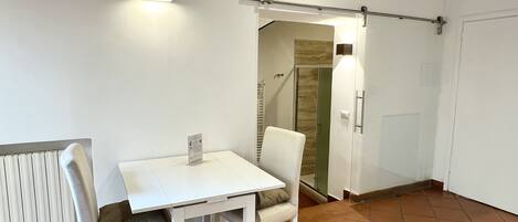 A small, clean room with a white table and chairs, a radiator, and a door leading to another room.