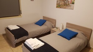 Two single beds with blue pillows and folded white towels, a nightstand with a lamp, and a wall-mounted picture of a bicycle. - Etna Parking (Catania)