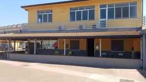 A two-story building with a yellow facade, a covered outdoor seating area, and a visible entrance. - Etna Parking (Catania)
