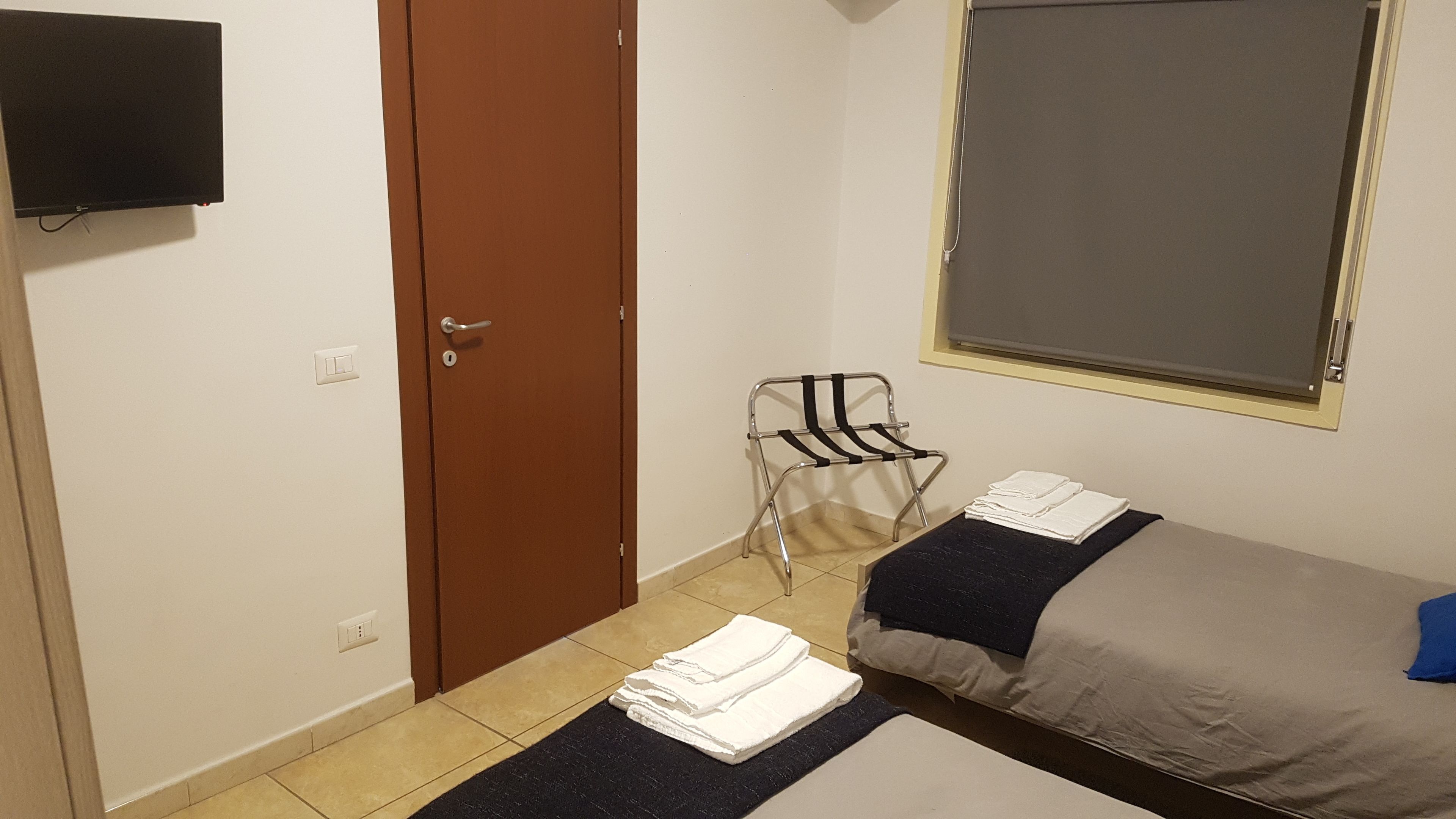 Une petite pièce propre, avec un lit, une chaise, une télévision et une fenêtre.