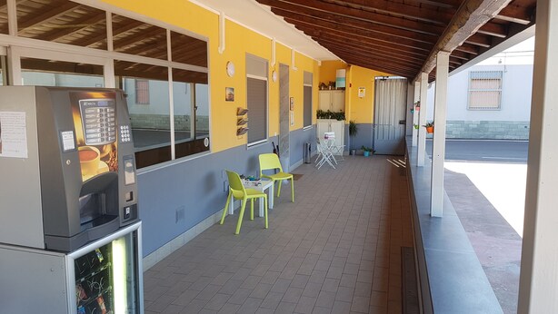 A covered outdoor seating area with a vending machine, chairs, and a small table. - Etna Parking (Catania)