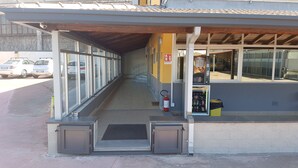 A building entrance with a covered walkway, a fire extinguisher, a vending machine, and a car parked outside. - Etna Parking (Catania)