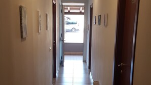 A hallway with a tiled floor, doors on both sides, and a view of a vehicle outside. - Etna Parking (Catania)