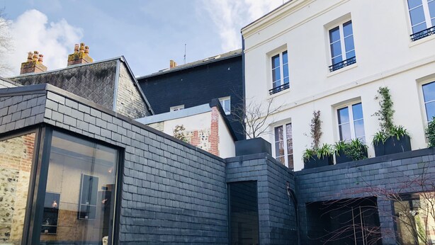 Ein modernes Gebäude mit Glasfassade, Backsteinfassade und einem kleinen Gartenbereich mit Bank und Blumentöpfen.