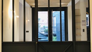 Ein modernes Interieur mit einer Holzschubladen Decke, einer schwarzen Tür mit geometrischem Muster und Blick auf ein Backsteinhaus.