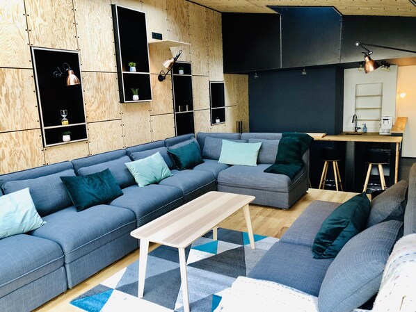Un salon moderne avec un canapé d’angle, une table basse en bois et des étagères intégrées ornées de plantes.