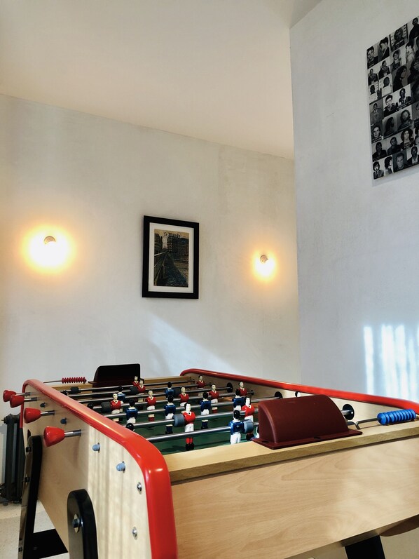 Una mesa de fútbol de mesa en una habitación con un cuadro enmarcado en la pared y dos luces fijadas a la pared.