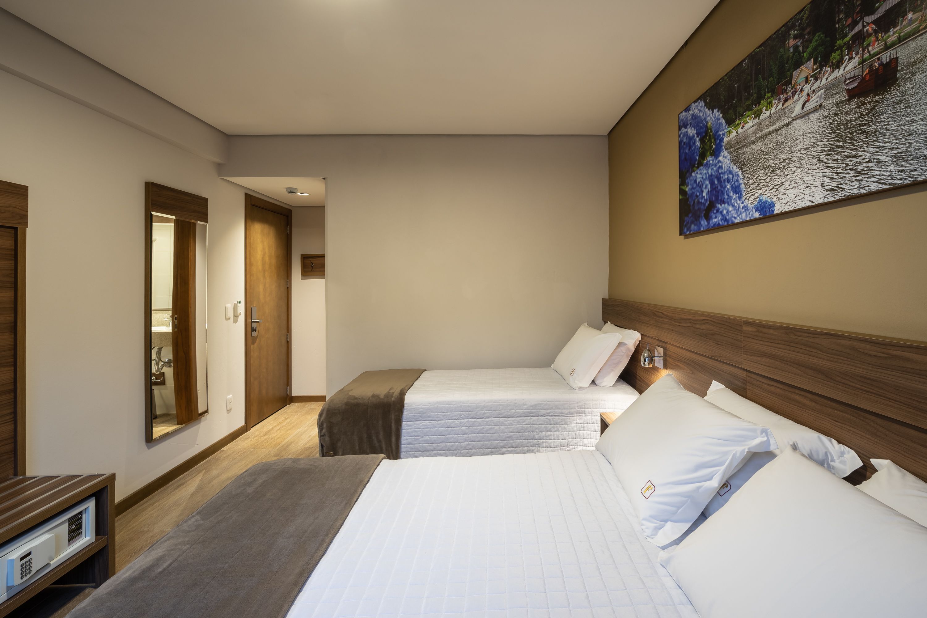 Habitación de hotel con dos camas, cabecero de madera, un ventanal grande y un cuadro en la pared.