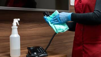 Una persona con uniforme rojo limpiando un escritorio de madera con un atomizador y un teléfono.