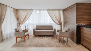 A modern living room with a beige sofa, two armchairs, a coffee table, and a wooden accent wall. - Hotel Fioreze Primo (Gramado)